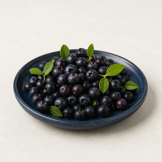 Small dark bilberries with green leaves on a navy ceramic plate
