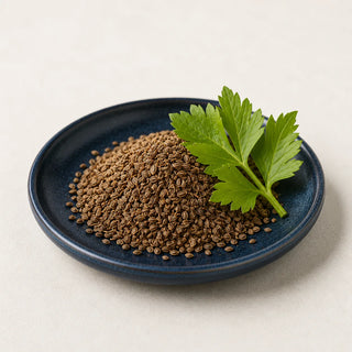 Mound of tiny brown celery seeds with a fresh celery leaf on a navy ceramic plate