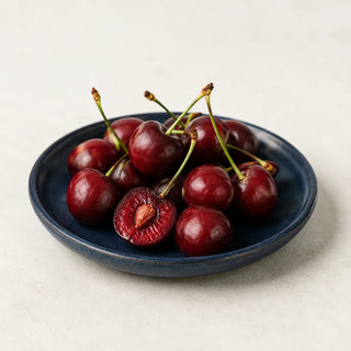 Dark red tart cherries with stems on a navy ceramic plate, one halved showing the pit